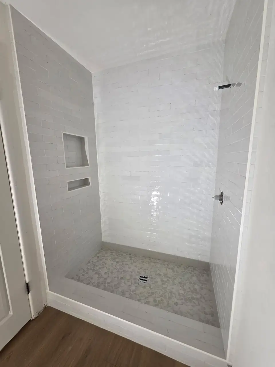 Walk-in shower by Inland Empire tile contractor JMR Tile & Stone: glossy white subway tile walls, two recessed niches and a pebble mosaic floor
