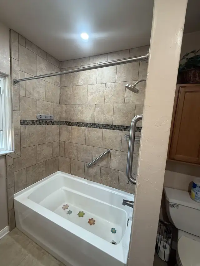 Bathtub surround in beige tile with a dark glass mosaic accent band and chrome grab bars